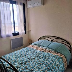 ein Schlafzimmer mit einem Bett mit blauer Decke und einem Fenster in der Unterkunft Le Bel Air in Canet-en-Roussillon