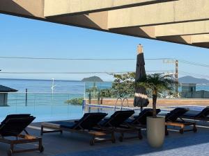 - une piscine avec des chaises longues, un parasol et l'océan dans l'établissement Alto Padrão, Home Club, vista mar e Beto Carrero, à Balneário Piçarras