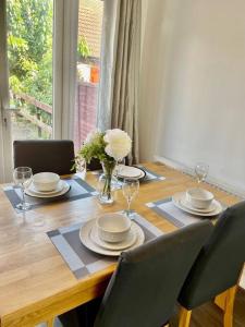 a dining room table with plates and glasses and a vase of flowers at The Herald House Dartford 3 Bedroom Apartment in Kent