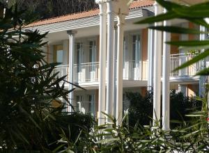 a white building with white columns and trees at Ville Lago Lugano in Porto Ceresio