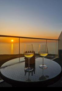 two wine glasses sitting on a table with a sunset in the background at Sea View Apartment at One Lusty Glaze in Newquay