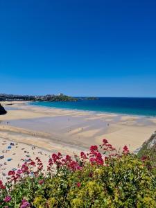 a beach with people walking on the sand and flowers at Sea View Apartment at One Lusty Glaze in Newquay