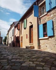 a building with blue shutters on a cobblestone street at CasAlice Room&Breakfast in centro storico in Santarcangelo di Romagna