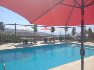 a swimming pool with a red umbrella and tables and benches at Sultana Farm and Villa in Bayyūḑah
