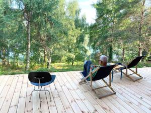 um homem sentado numa cadeira num deque de madeira em Lunette Lodge am See mit Sauna für 10 Gäste em Brzozie