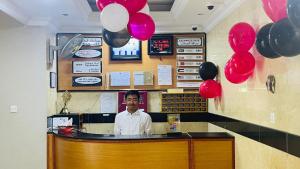 a man standing behind a counter with red and black balloons at Al Ghadeer Hotel Apartment in Sharjah