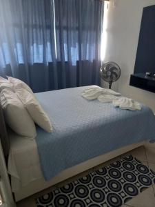 a bed with white sheets and pillows and a fan at Apartamento 1010 in Goiânia