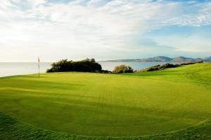 a green golf course with the ocean in the background at Due Lune Puntaldia Resort & Golf in San Teodoro