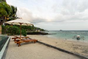 a beach with two benches and an umbrella at Utama Villas Beach Front Candidasa in Candidasa