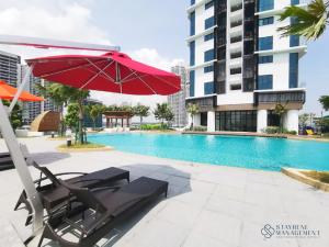 a red umbrella and chairs next to a swimming pool at Almas Suites Puteri Harbour by Stayrene in Nusajaya