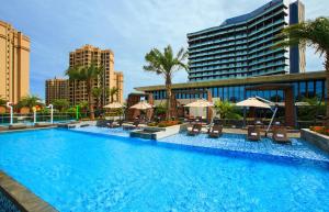 海口的住宿－海口萬麗酒店，一座带椅子和遮阳伞的游泳池位于一座建筑旁边