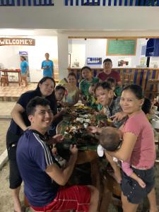 eine Gruppe von Menschen, die um einen Tisch mit einem Teller Essen stehen in der Unterkunft Baie Benie Beach Resort in Balibago