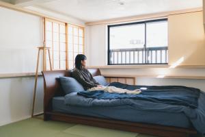 una donna seduta su un letto in una stanza con finestra di 竹田まちホテル a Taketa