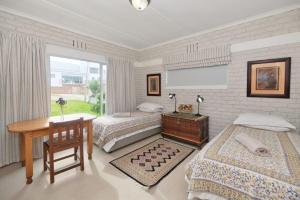 1 dormitorio con 2 camas, escritorio y ventana en Oceanview House, en Struisbaai