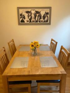 a wooden table with a vase of flowers and two cows at Little Nest EV Point in Wadebridge