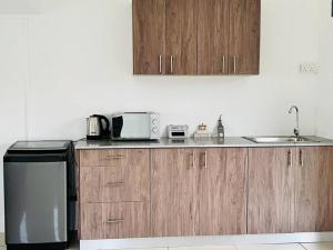 eine Küche mit Holzschränken, einer Spüle und einer Mikrowelle in der Unterkunft Green Village Duplex in Grand-Gaube