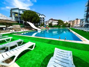 a swimming pool with green grass and white chairs at Hotel First Class Didim in Didim