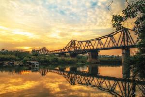 uma ponte ferroviária sobre um rio com um pôr-do-sol em Marigold Hotel Hanoi em Hanói