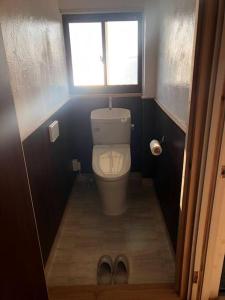 a bathroom with a toilet with a window and a pair of shoes at Cliff top Terrace in Kuranomoto