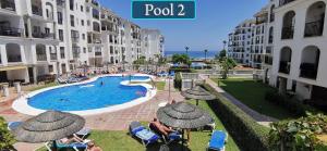 a resort pool with people sitting in chairs and umbrellas at Puerto de la Duquesa Sea Views in Manilva