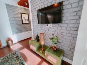 a living room with a tv on a white brick wall at Eco Farmstay Cottages #1 in Dharamshala