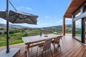 um deque de madeira com uma mesa e um guarda-chuva em Vino and Views - Bannockburn Holiday Home em Cromwell