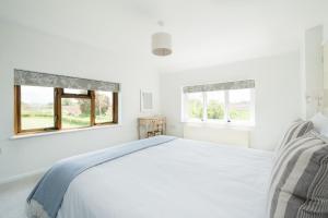 a white bedroom with a bed and two windows at Wye Valley Holiday Cottage - Field Cottage in Peterstow