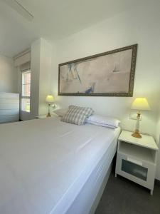 a white bedroom with a large white bed and two lamps at Seaside Apartment Retreat in Benicàssim