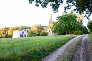 un camino de tierra que conduce a un campo con una casa en Les Perroutis, en Saint-Alvère