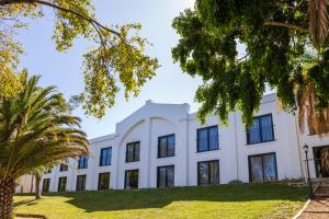 einen Blick nach außen auf ein weißes Gebäude mit Bäumen in der Unterkunft Lord Charles Hotel in Somerset West