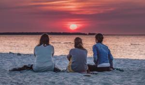 トラッセンハイデにあるHotel Kaliebeの三人の女性が夕日を眺めながら海辺に座っている