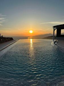 uma piscina de beiral infinito com o pôr-do-sol ao fundo em White Rock Suites & Villas em Houlakia