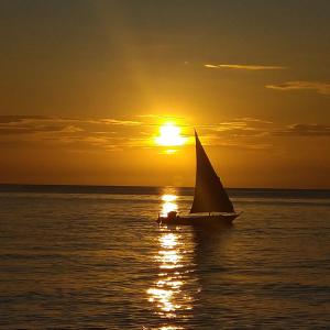 a sail boat in the ocean at sunset at Furaha B&B Kendwa in Kendwa