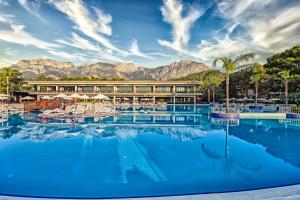 a hotel with a large pool with mountains in the background at Kimeros Park Holiday Village - Ultra All Inc. Kids Concept in Kemer