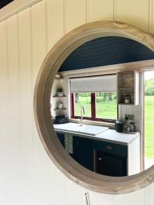 a mirror in a kitchen with a sink and a window at Cleo’s Hut in Cowfold