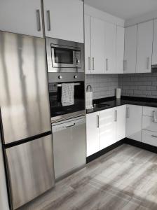 una cocina con armarios blancos y electrodomésticos de acero inoxidable en Piso marinero, en Muxía
