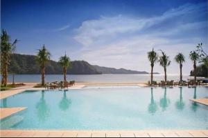 a large swimming pool with palm trees and a beach at Seanna's Place at Pico de Loro in Nasugbu