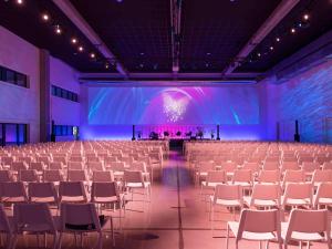 una sala de banquetes vacía con sillas blancas y una pantalla grande en ibis Styles Namur en Namur