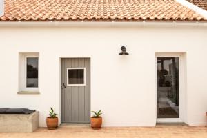 a white house with a gray door and two potted plants at Vida na Aldeia in São Luis