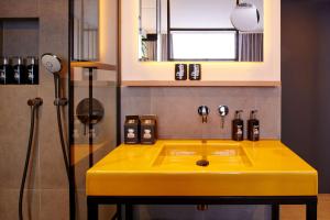 a yellow sink in a bathroom with a shower at me and all hotel Ulm, part of JdV by Hyatt in Ulm