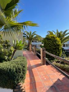 a brick walkway with palm trees and a fence at Jardines Apartment in Sitio de Calahonda