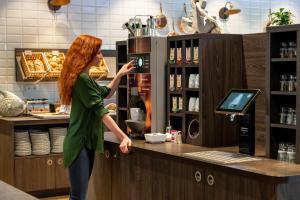 a woman standing at a counter with a coffee machine at ibis Styles Hamburg Barmbek in Hamburg