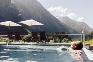 a woman in a swimming pool with mountains in the background at Hotel Weisseespitze in Kaunertal