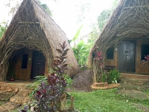 two small houses with thatched roofs in a garden at Sumilir Riverside Retreat in Banyuwangi