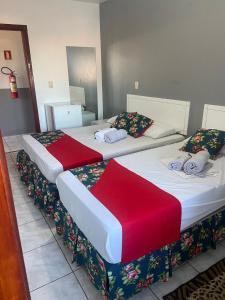 two beds in a hotel room with red and white sheets at Teuthos Hotel in Teutônia