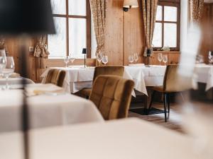 un restaurante con mesas y sillas blancas y ventanas en Almwellness-Resort Tuffbad, en Sankt Lorenzen im Lesachtal