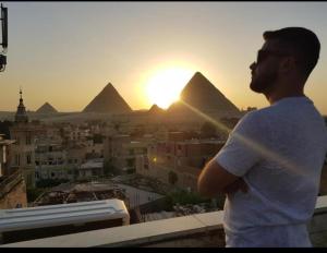 een man die bovenop een gebouw staat en naar de piramides kijkt bij City pyramids inn in Caïro