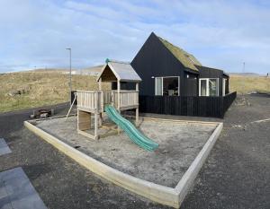 un parque infantil con una casa negra y un tobogán en Captains Cottage, en Sandur