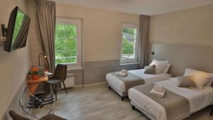 a hotel room with two beds and a desk and two windows at L'HÔTEL DES BAINS - Salles-la-Source in Salles-la-Source