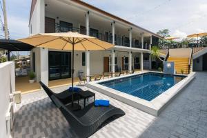 una piscina con sillas y una sombrilla junto a un edificio en The Chu’s Boutique Hotel, en Khao Lak